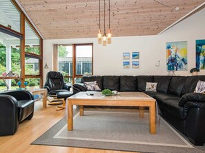Un soggiorno moderno con soffitto in legno, divani in pelle, un tavolino da caffè e ampie finestre che si affacciano sul verde.