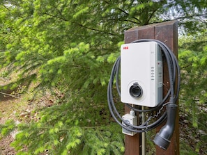 Caixa elétrica externa com um cabo conectado, com folhagem verde ao fundo.