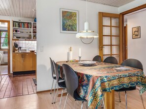 A dining area with a table set for four, chairs, a patterned tablecloth, a hanging light fixture, and a bookshelf in the background. - 6 Person Holiday Home in Ronne (Ronne)