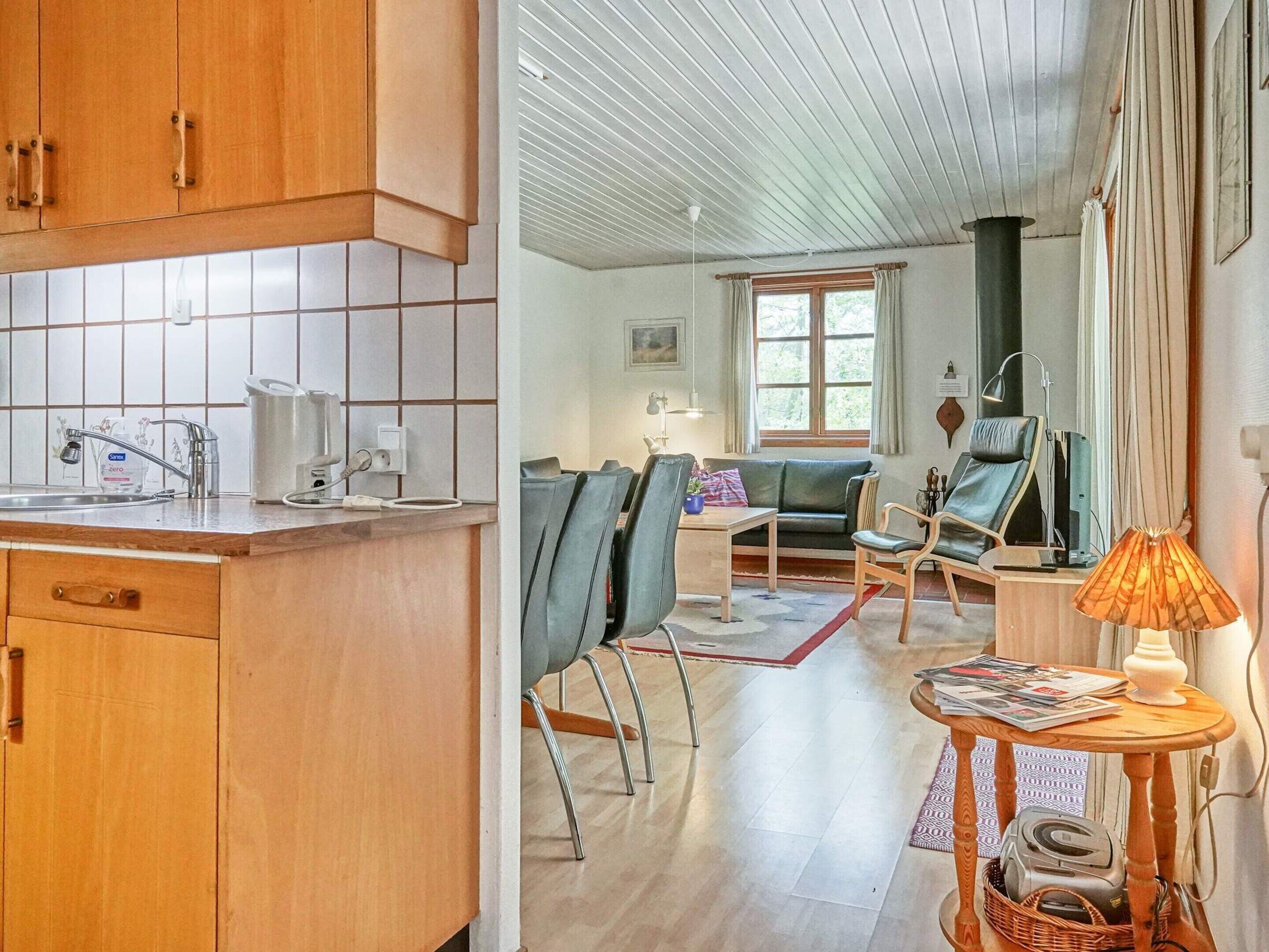 Una cocina con armarios de madera y salpicadero de azulejos, un comedor con mesa y sillas, y una sala de estar con sofá y lámpara.