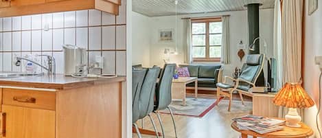Una cocina con armarios de madera y salpicadero de azulejos, un comedor con mesa y sillas, y una sala de estar con sofá y lámpara.