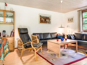A living room with a sofa, a wooden coffee table, a chair, a cabinet with glass doors, and a window with curtains.