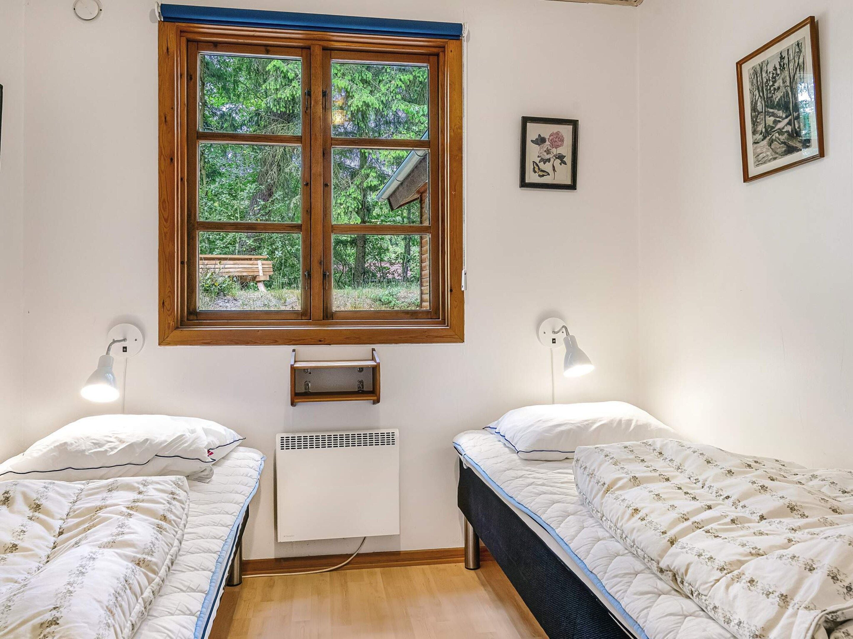 A room with two single beds, a window with a view of greenery, a wall-mounted heater, and two wall-mounted lamps.