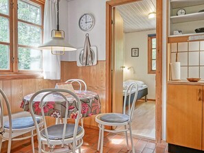 Ein Zimmer mit einem Holztisch, Stühlen, einem Bett, einer Uhr und einem Fenster mit Vorhängen.