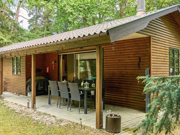A wooden cabin with a covered patio, a dining table with chairs, and a grill outside.
