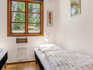A bedroom with a single bed, a window with a view of trees, a wall-mounted light, and a framed picture.