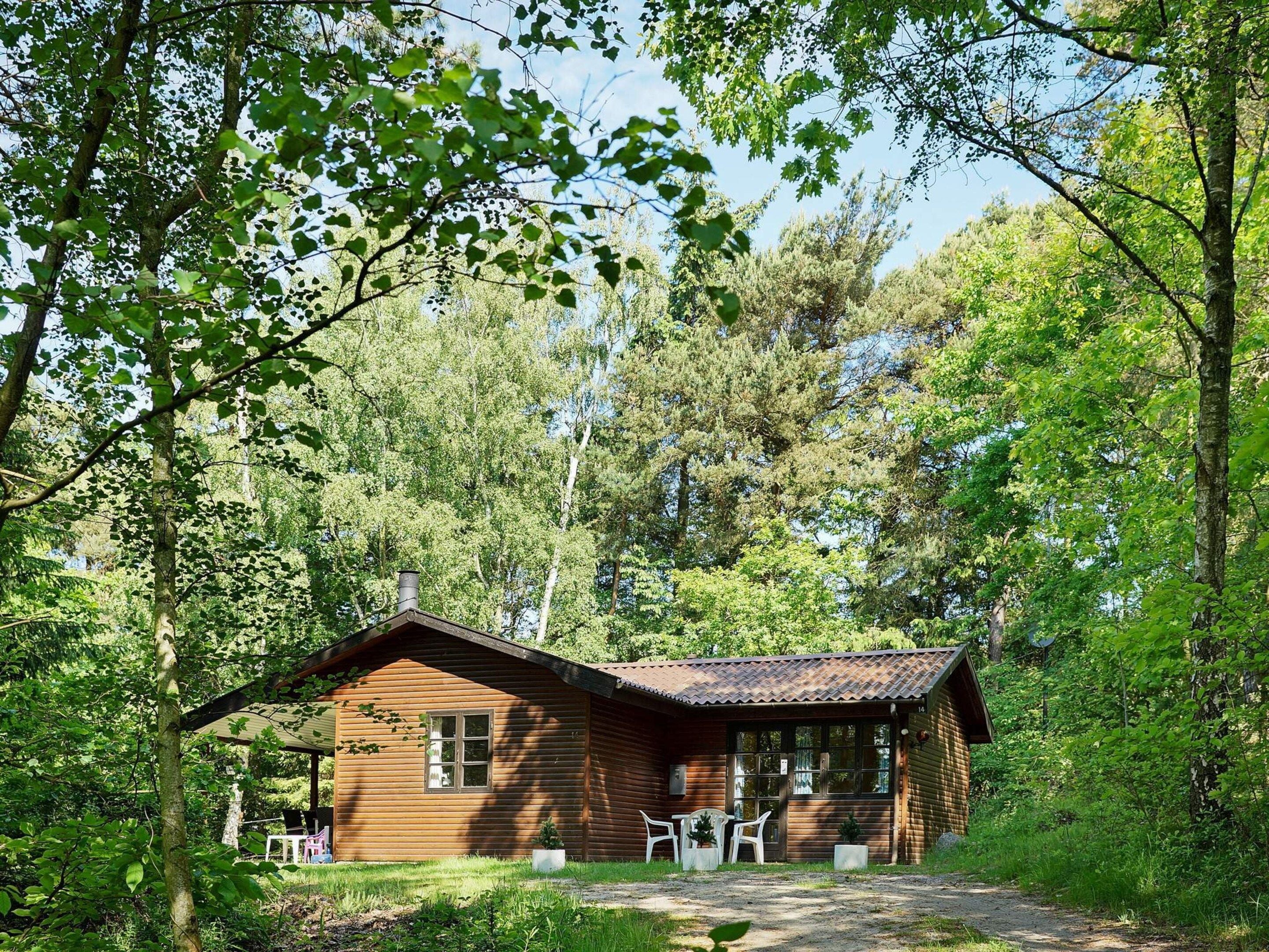 A wooden cabin with a porch and two chairs, surrounded by dense forest.
