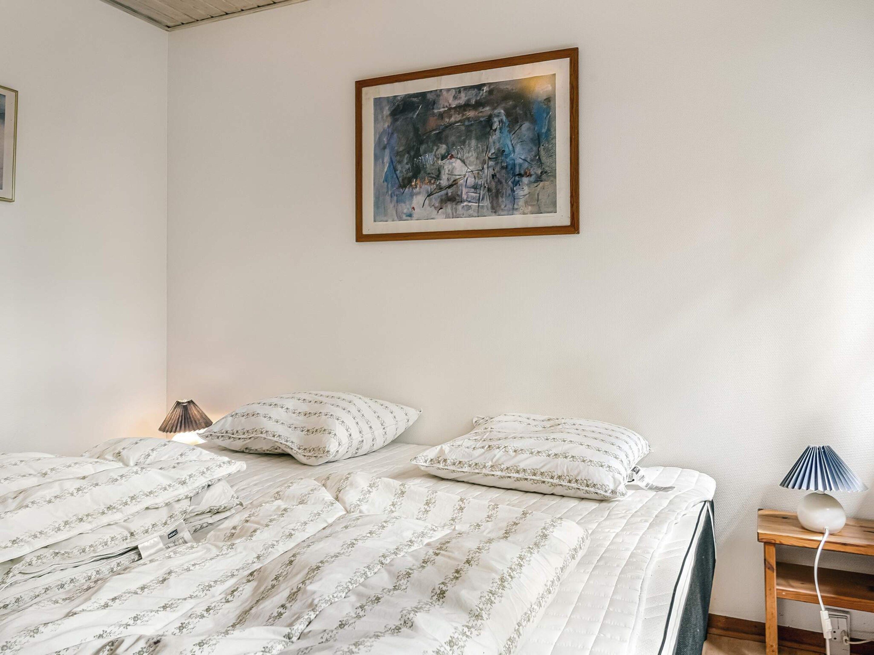 A bedroom with a bed, pillows, a bedside lamp, and a wall-mounted painting.