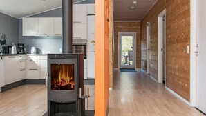 A modern kitchen with a wood-burning stove, white cabinets, and a wooden interior. - Spacious Cottage in Harboøre With Sauna (Harboore)