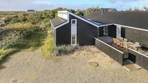 A modern house with a sloped roof, a deck with outdoor furniture, and a gravel driveway. - Spacious Cottage in Harboøre With Sauna (Harboore)