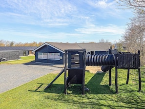 A playground with a slide and climbing structure, a building with a dark roof, and a grassy area.