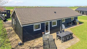 Una casa moderna con tejado de baldosas, un patio con mobiliario exterior y vistas al campo.
