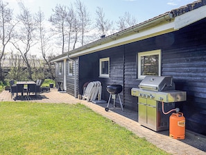 A house with a barbecue grill and a gas tank outside.