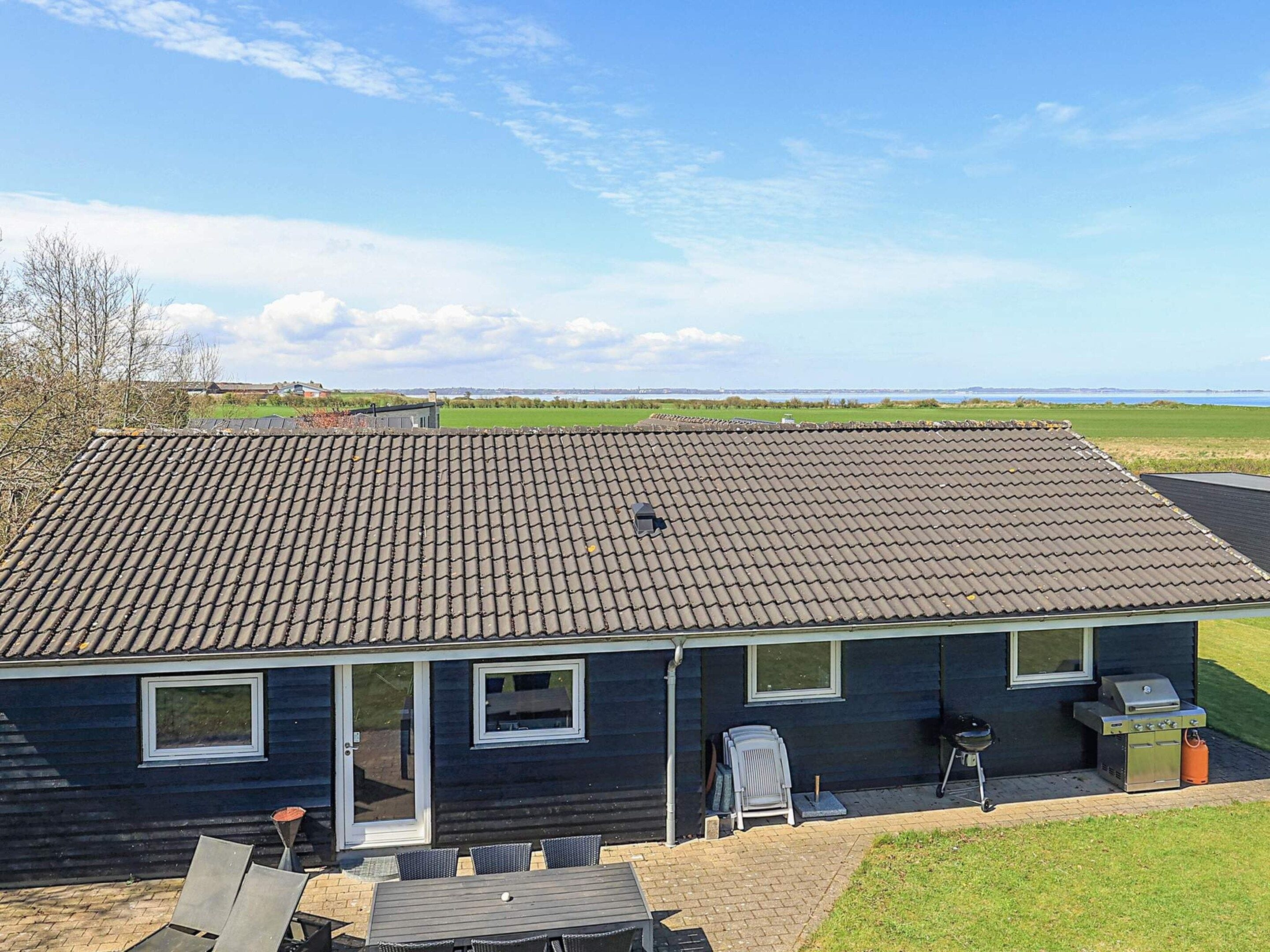 A house with a tiled roof, a patio with a table and chairs, and a grill area.