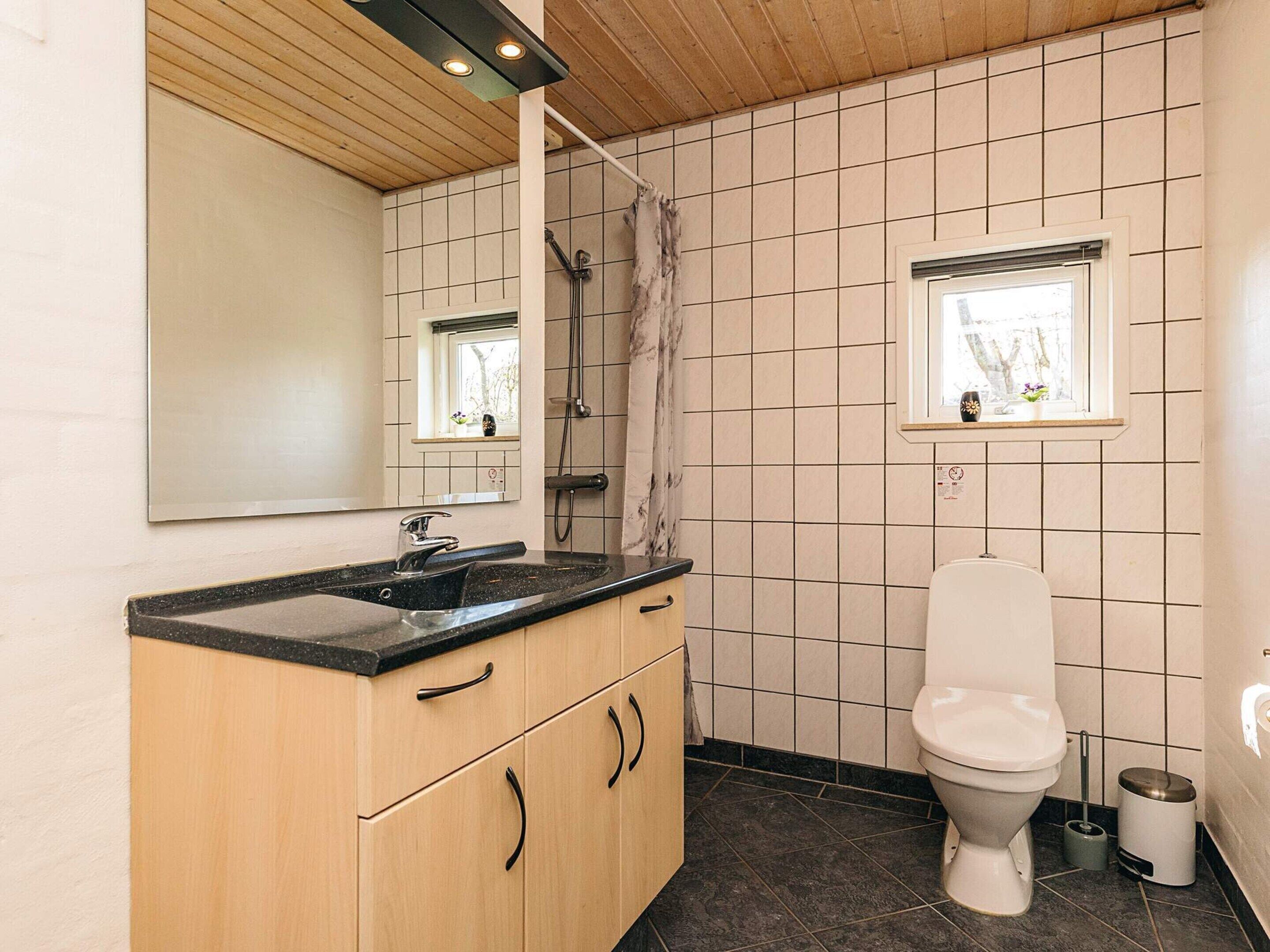 A bathroom with a toilet, sink, mirror, shower, and a window with a view.