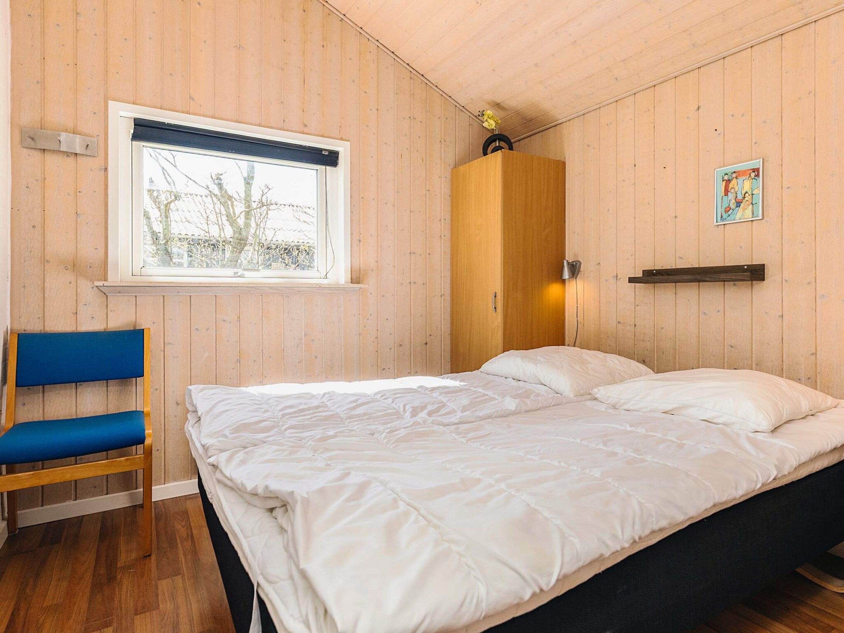 Ett rum med en säng, en stol, ett fönster och en garderob i trä.