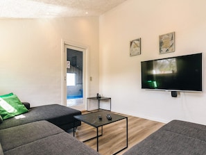 A modern living room with a flat-screen TV, grey sofas, a small coffee table, and a door leading to a balcony.