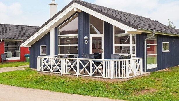 A single-story house with a dark blue exterior, a white porch with a railing, and a chimney. - Holiday Home in Grossenbrode (Grossenbrode)