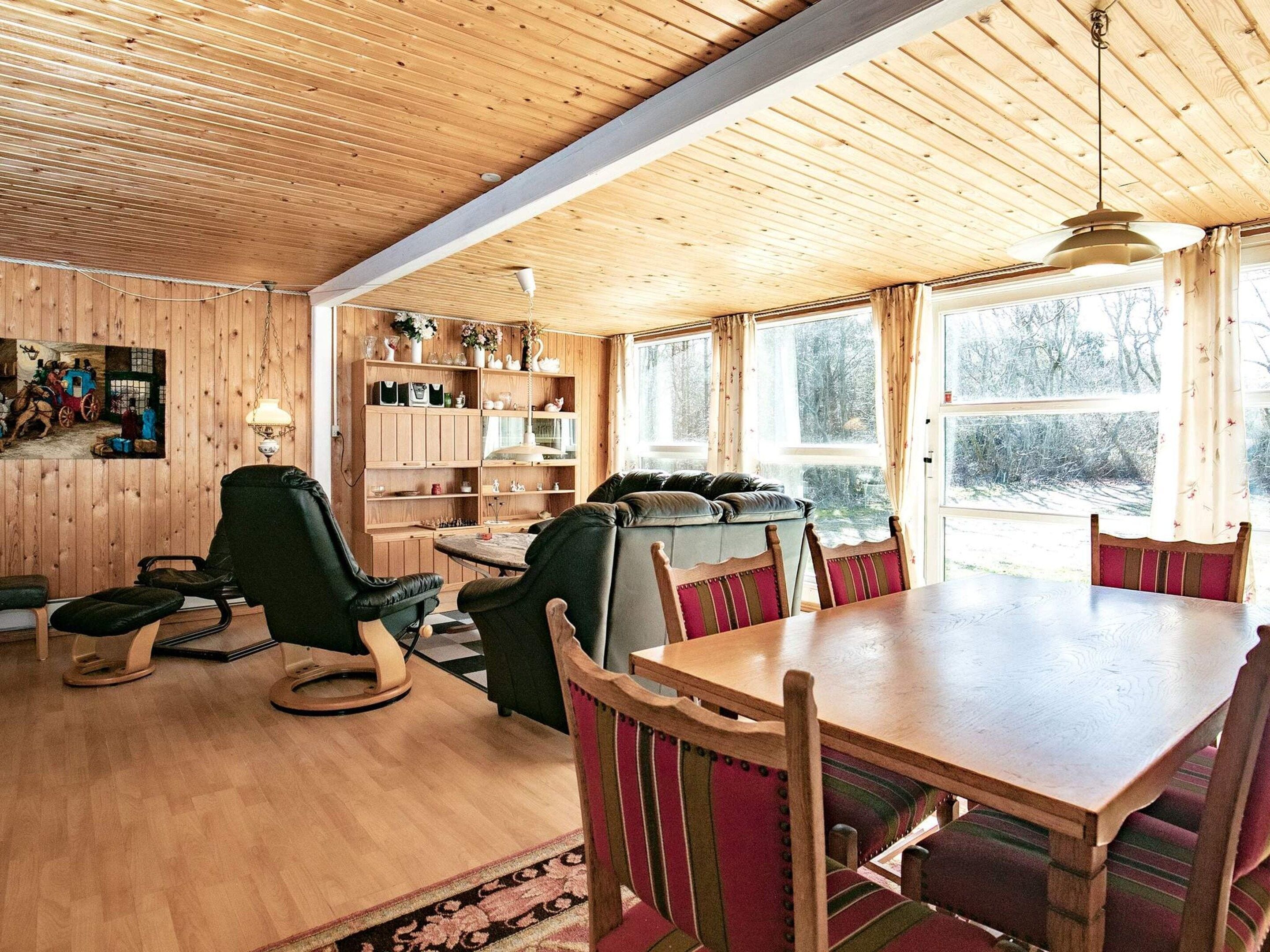 A cozy room with a wooden ceiling, a dining table with chairs, a sofa, and a bookshelf.