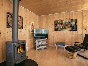 A cozy room with a wood-burning stove, a television on a stand, and a comfortable chair.
