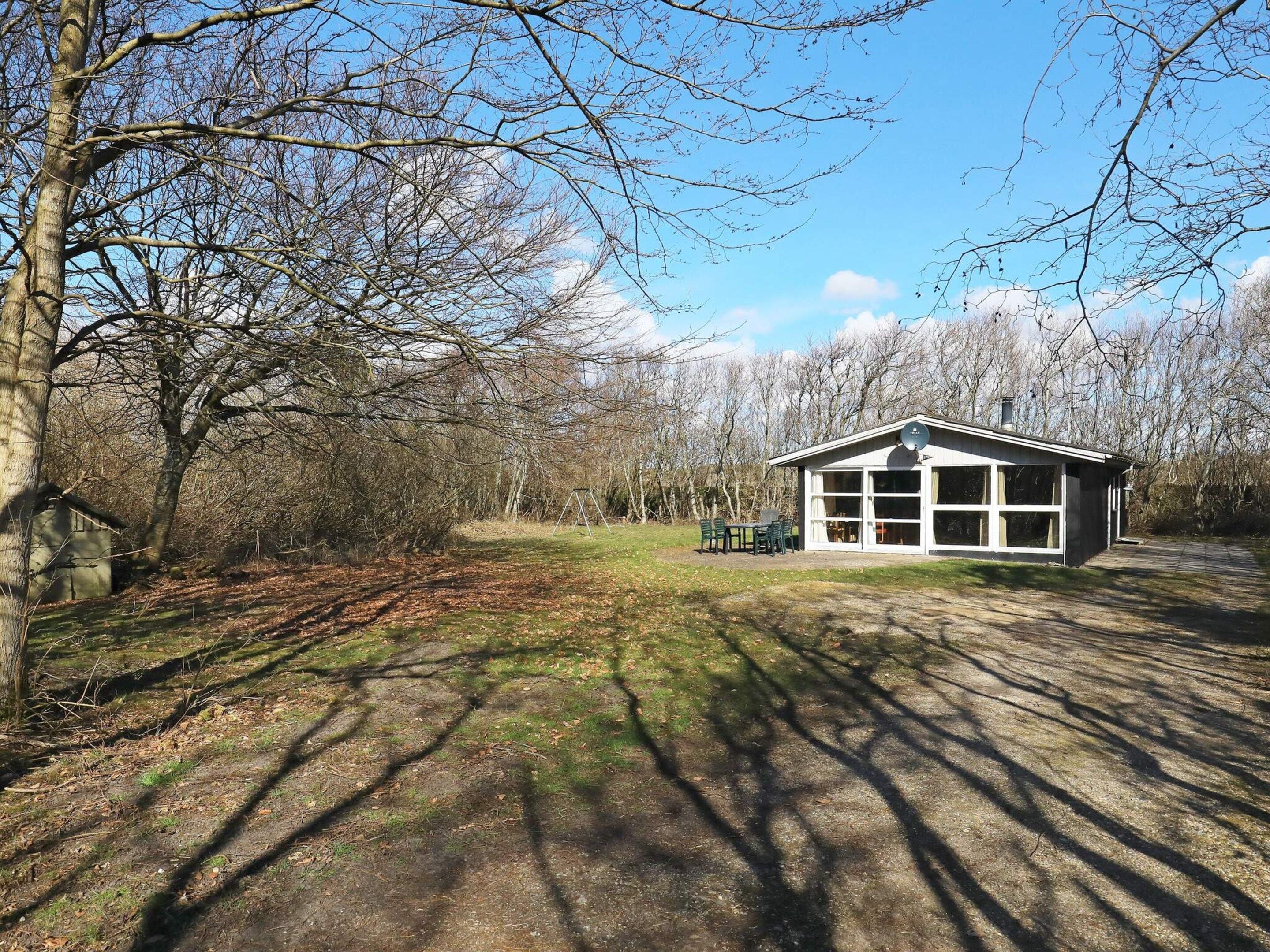 A small, single-story building with large windows, surrounded by trees and a grassy area.