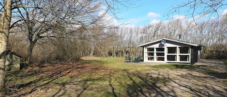 A small, single-story building with large windows, surrounded by trees and a grassy area.