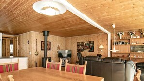 Um quarto com painéis de madeira, uma mesa de jantar, cadeiras, um sofá e uma televisão.