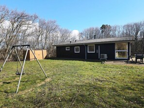 Ein kleines Haus mit einem umzäunten Garten, einer Schaukel und einem Geräteschuppen.