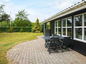 Eine Terrasse mit Tisch und Stühlen, einem Heckenstreifen und einem Baum.