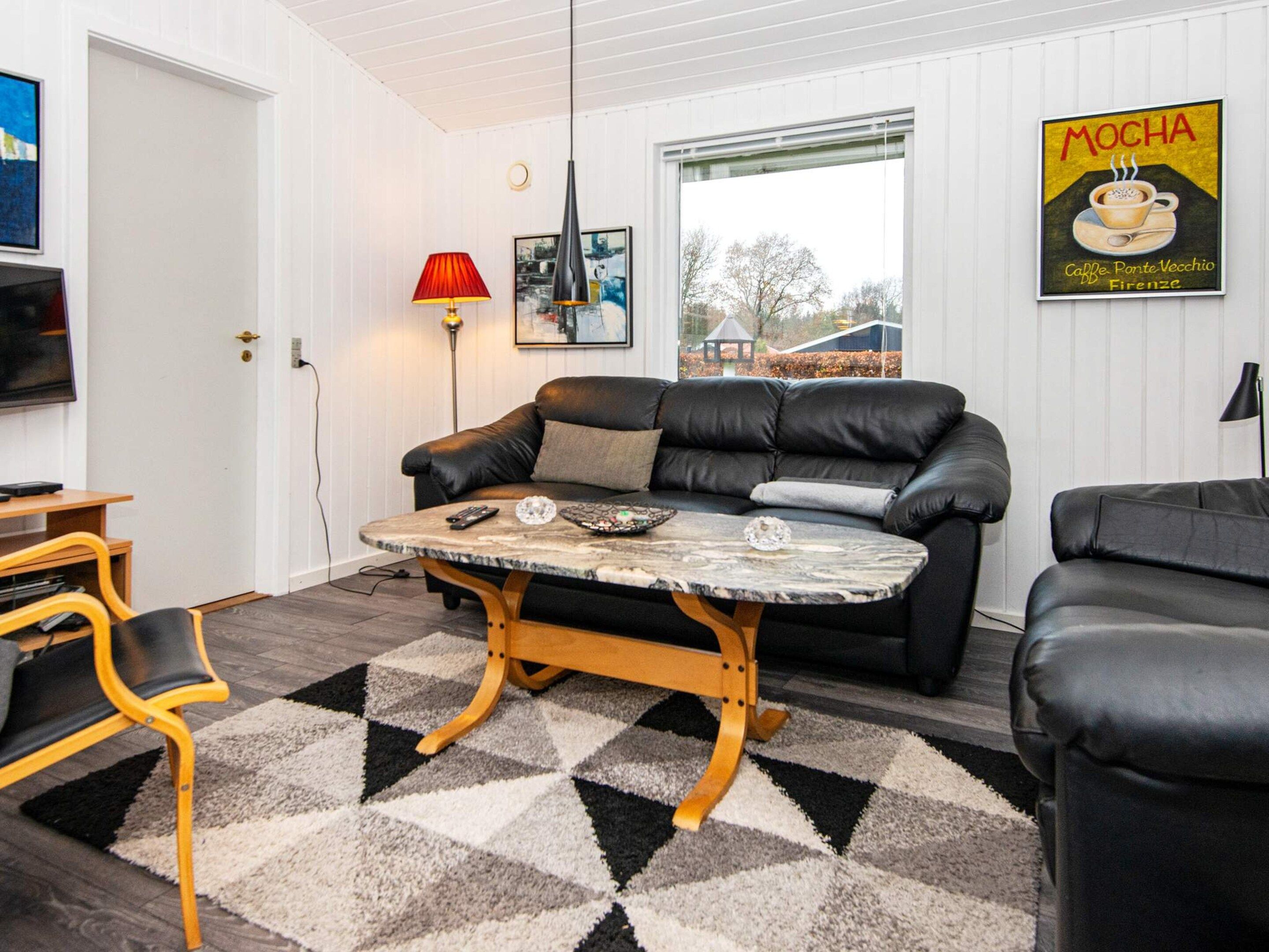 A living room with a black leather sofa, a round coffee table, a red floor lamp, and a wall-mounted television.