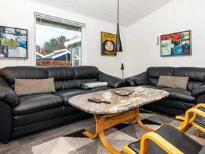 A modern living room with two black leather sofas, a round coffee table, and a wooden bench.