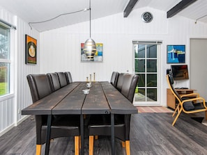 A conference room with a long table, black leather chairs, a hanging pendant light, and a television on a stand.