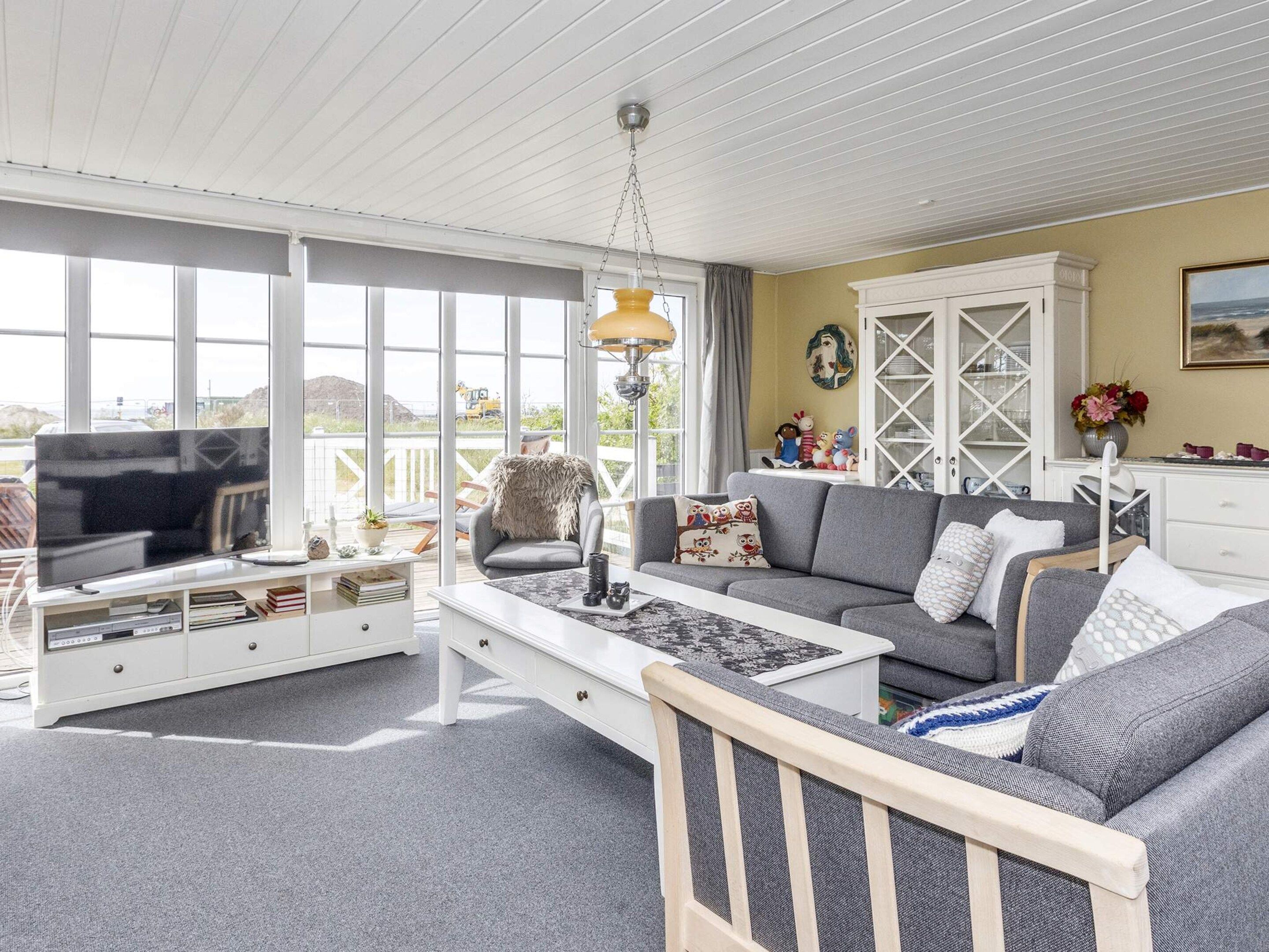 A spacious living room with a large window, a television, a sofa, a coffee table, and a white cabinet.