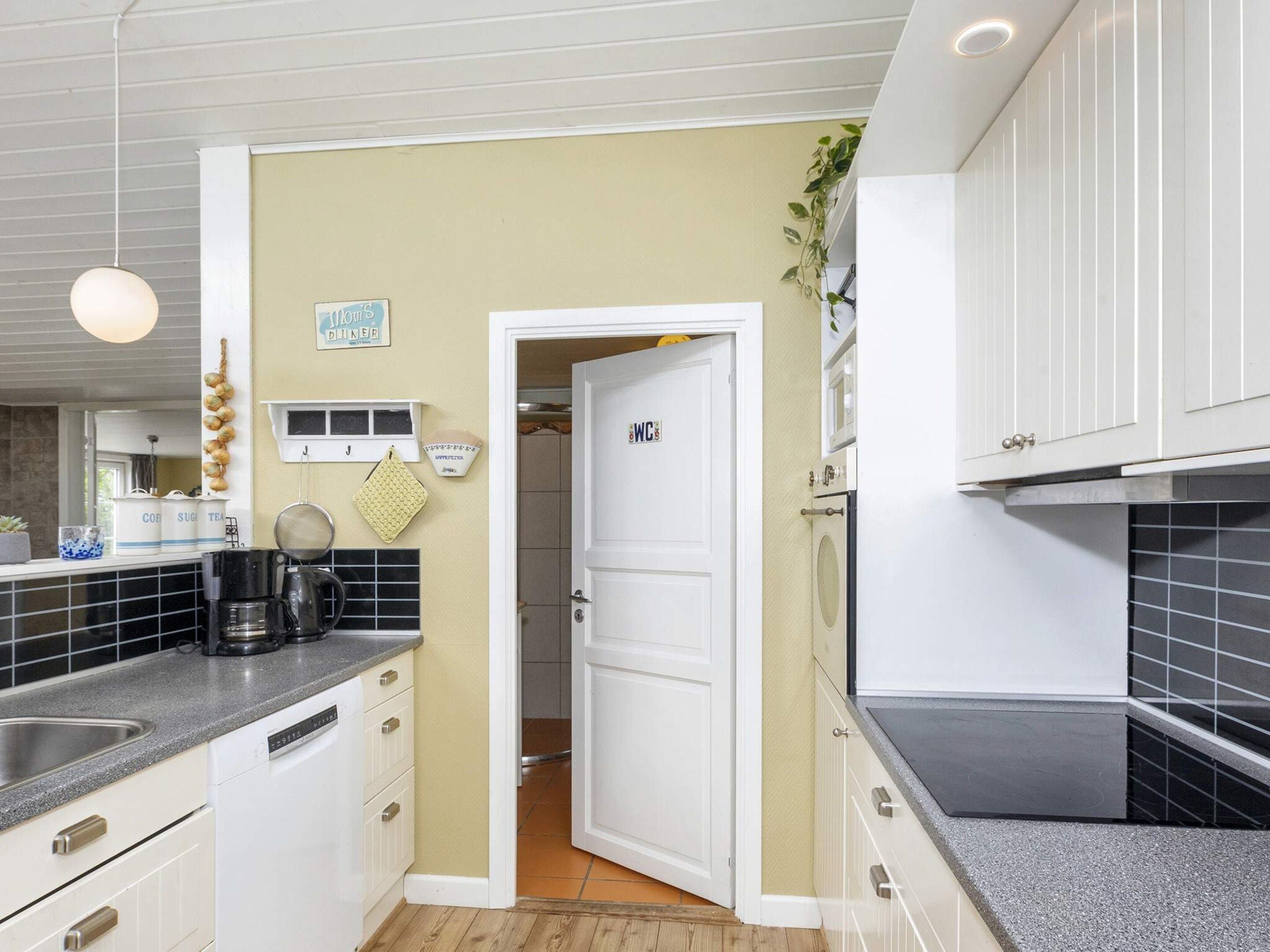 A compact kitchen with white cabinetry, a coffee machine, and a sign indicating a dining area.