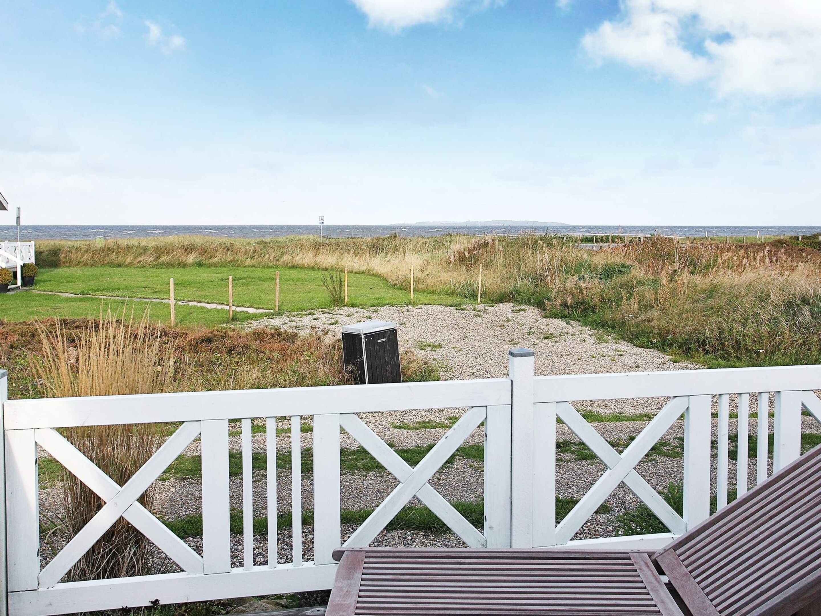 A deck with a view of a grassy field and a distant shoreline.