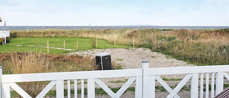 A deck with a view of a grassy field and a distant shoreline.
