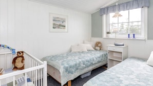 A child's bedroom with two beds, a crib, a desk, and a window with a view.