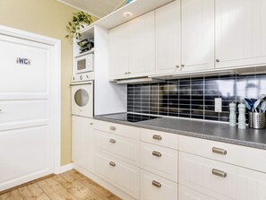 Een keuken met witte kastjes, een zwarte spatwand en een magnetron.