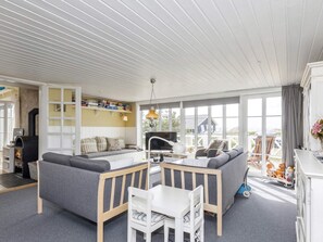 Een ruime woonkamer met een bank, een eettafel en een televisie. Er is een open haard en een raam met uitzicht.