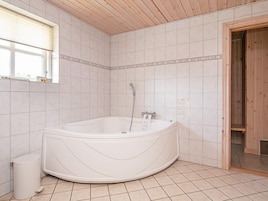 A bathroom with a freestanding bathtub, tiled walls, a window, and a wooden ceiling.