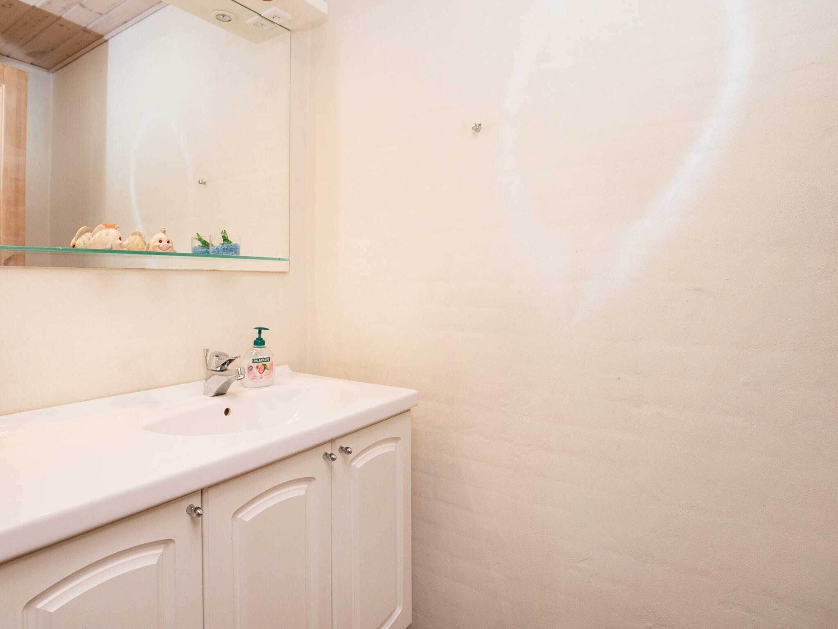 A bathroom with a white sink, a mirror, and a shelf with decorative items.