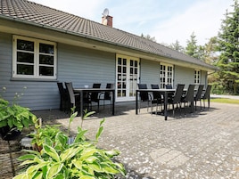 A house with a patio area featuring a table and chairs, surrounded by greenery.