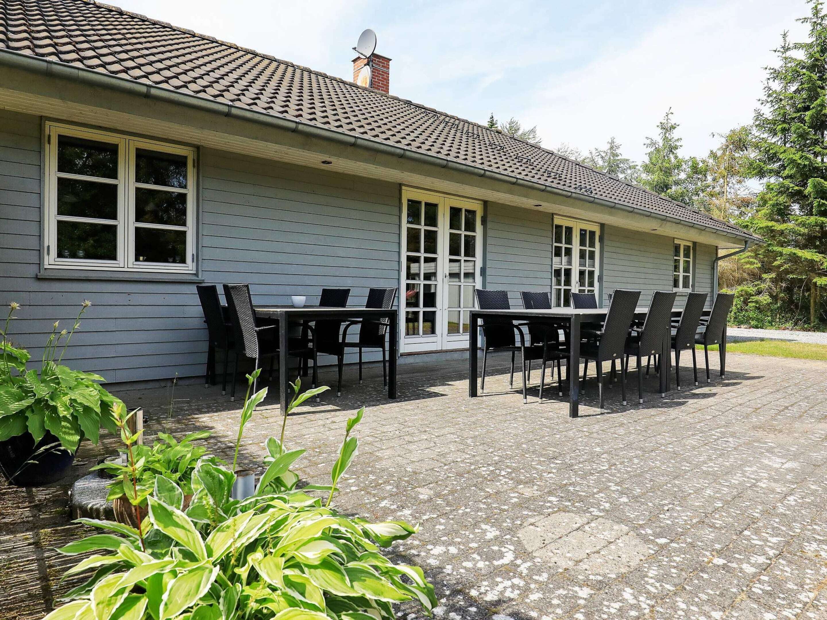A house with a patio area featuring a table and chairs, surrounded by greenery.