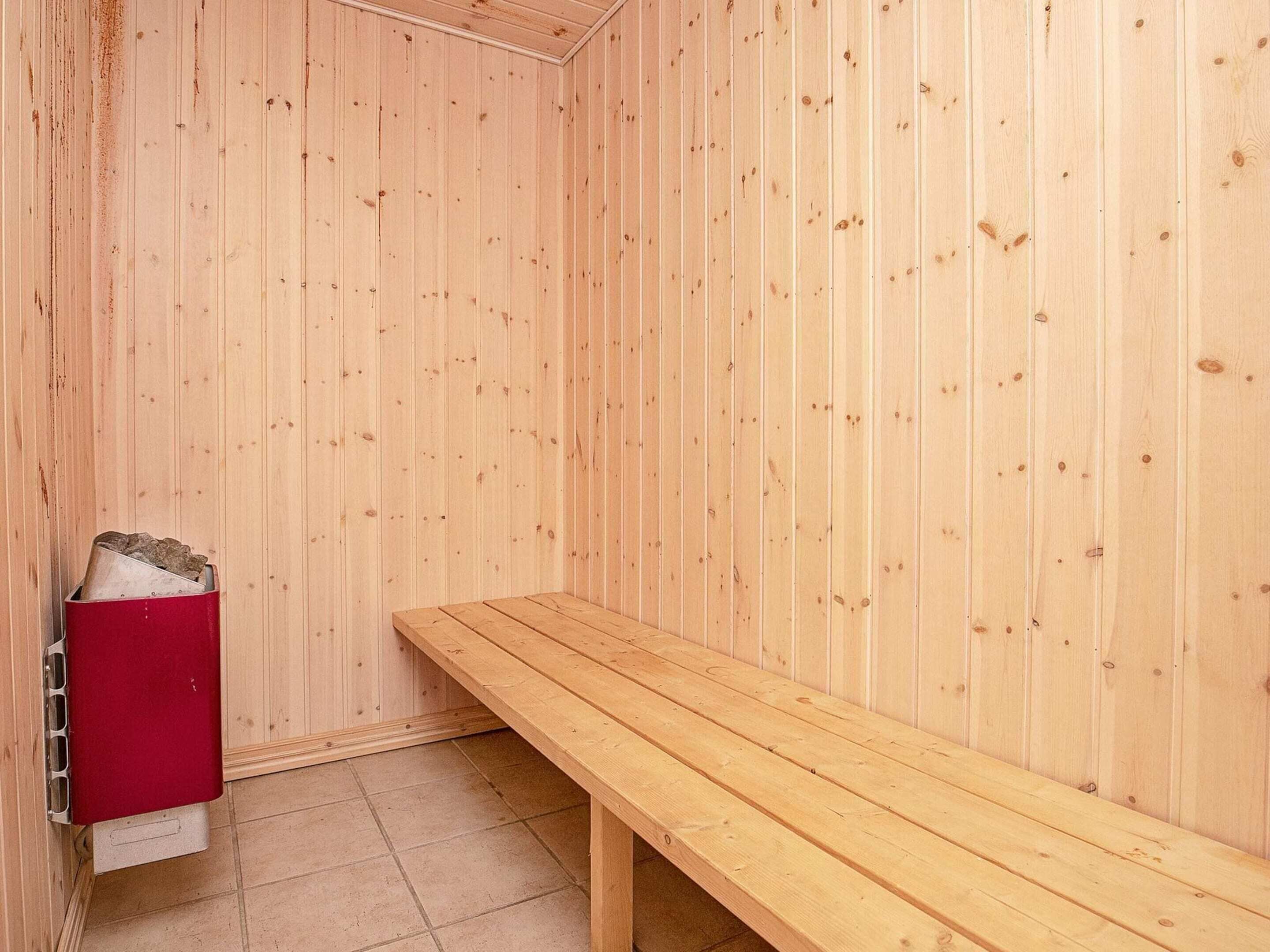 A sauna room with wooden walls, a bench, and a red heater.