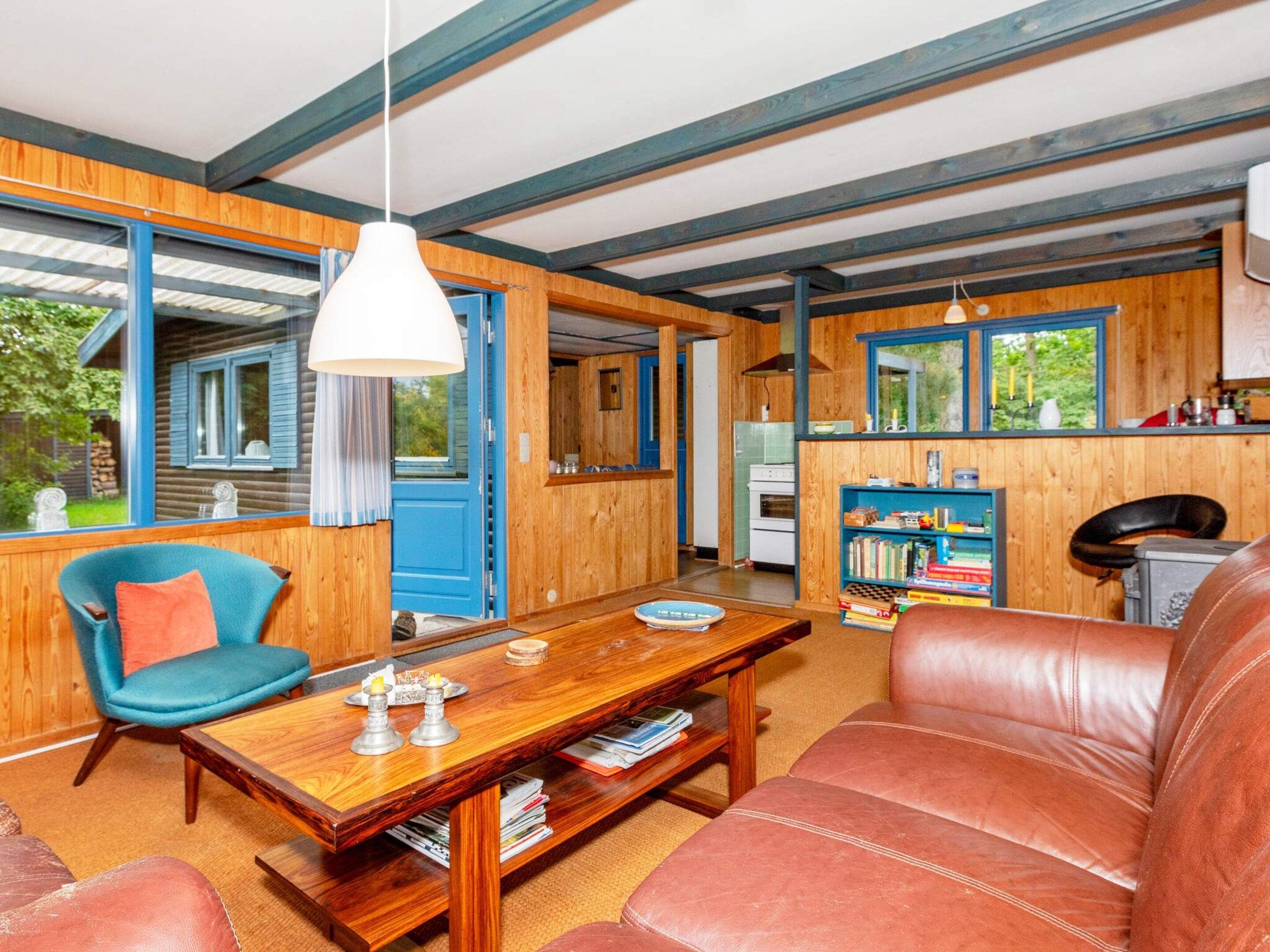 Une pièce chaleureuse avec un plafond en bois, une chaise bleue, un canapé en cuir, une table en bois et une bibliothèque.