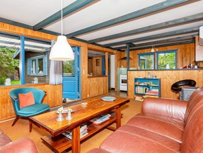 A cozy room with a wooden ceiling, a blue chair, a leather sofa, a wooden table, and a bookshelf.