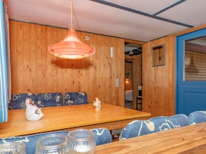 Interior de fusta amb taula i bancs, llum penjant i una porta amb finestreta.