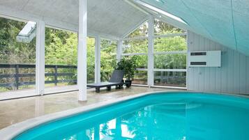 Una piscina techada con una banca y planta en maceta, rodeada de paredes de vidrio y columnas blancas.