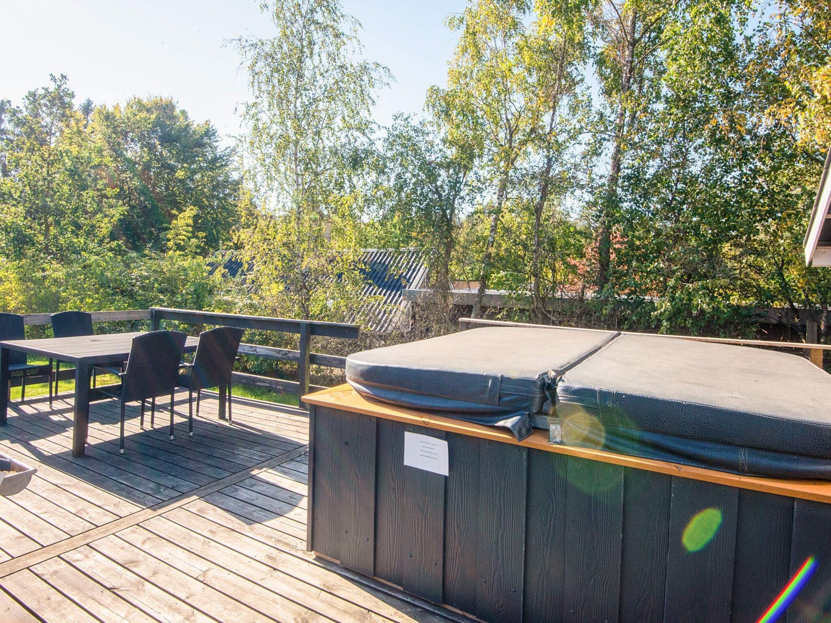 A wooden deck with a hot tub, outdoor seating, and a view of trees.