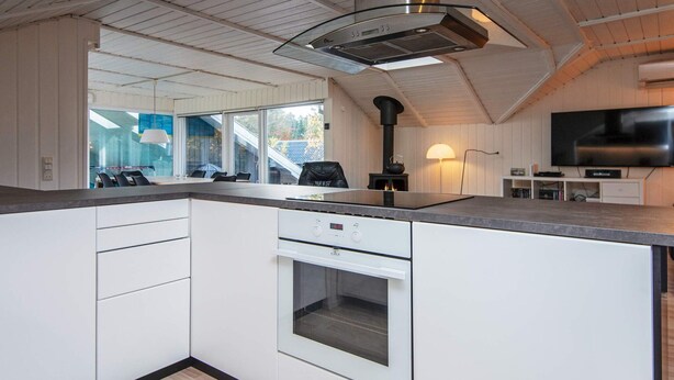 A modern kitchen with white cabinetry, a built-in oven, a stove, and a large window. - 6 Person Holiday Home in Ebeltoft (Ebeltoft)